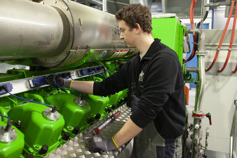 Industriearbeiter in Arbeitskleidung bedient Maschinen in einer Fabrikhalle, fokussiert auf die Einstellung eines großen grünen Maschinenteils