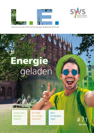 Cover der Ausgabe des "L.E. Magazins" mit der Überschrift "Energie geladen". Es zeigt eine fröhliche Person, die ein Selfie vor einem historischen Gebäude macht, mit grünem Laub im Hintergrund.
