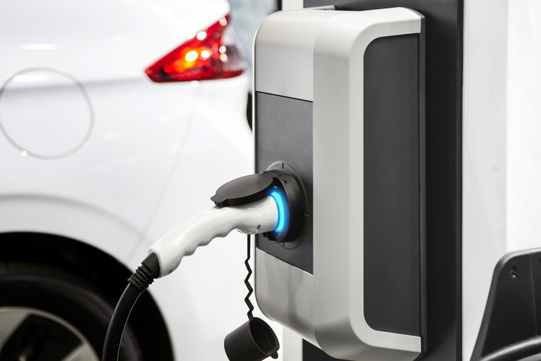 Ein weißes Elektroauto wird an einer modernen Ladestation aufgeladen, erkennbar am blau leuchtenden Stecker und Kabel, was den fortschrittlichen Trend zur Elektromobilität unterstreicht.