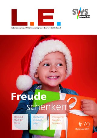Cover des "L.E. Magazins", Ausgabe 70, mit dem Thema "Freude schenken". Darauf ist ein lächelndes Kind mit einer Weihnachtsmannmütze zu sehen, das ein Geschenk hält, umgeben von einem festlichen roten Hintergrund.