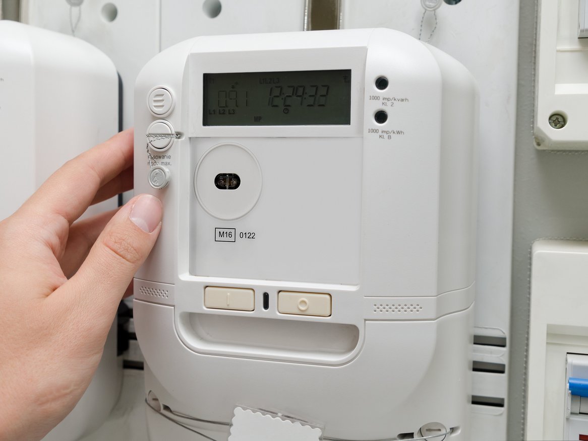 Eine Hand bedient einen modernen, weißen Thermostat an der Wand, einstellend oder ablesend, mit einer digitalen Anzeige und verschiedenen Steuerungsknöpfen.