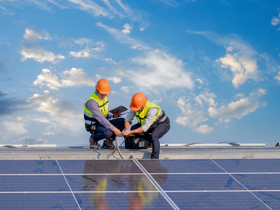 Zwei Ingenieure in Sicherheitskleidung arbeiten an der Wartung von Solarmodulen auf einem großen Solarfeld, mit einem dramatischen Himmel im Hintergrund, was die Verbindung von Technologie und Nachhaltigkeit veranschaulicht.