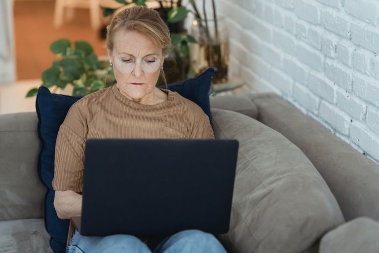 Ältere Drau sitzt auf der Couch und einen Laptop auf dem Schoß