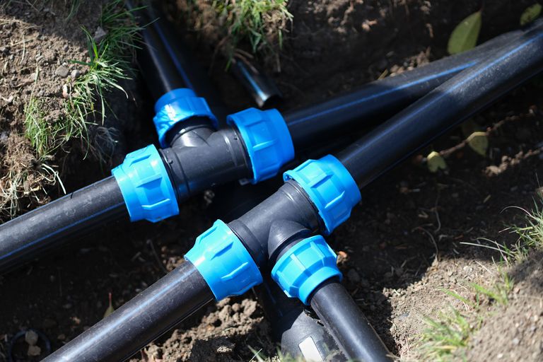 Schwarze Kunststoffrohre mit blauen Verbindungsstücken im Erdreich verlegt, vermutlich für Wasser- oder Bewässerungssysteme.