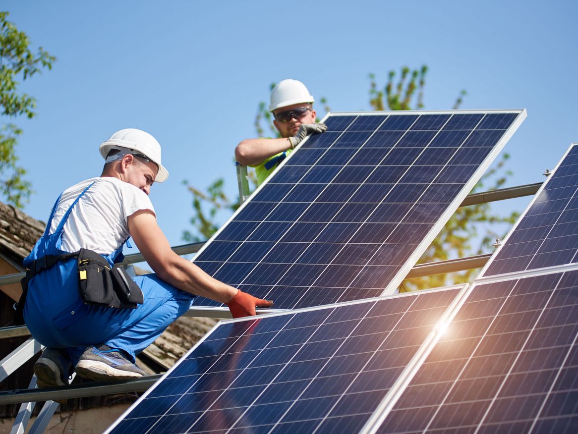 Das Bild zeigt die Montage eines Solarmoduls auf einem Dach mit zwei Arbeitern