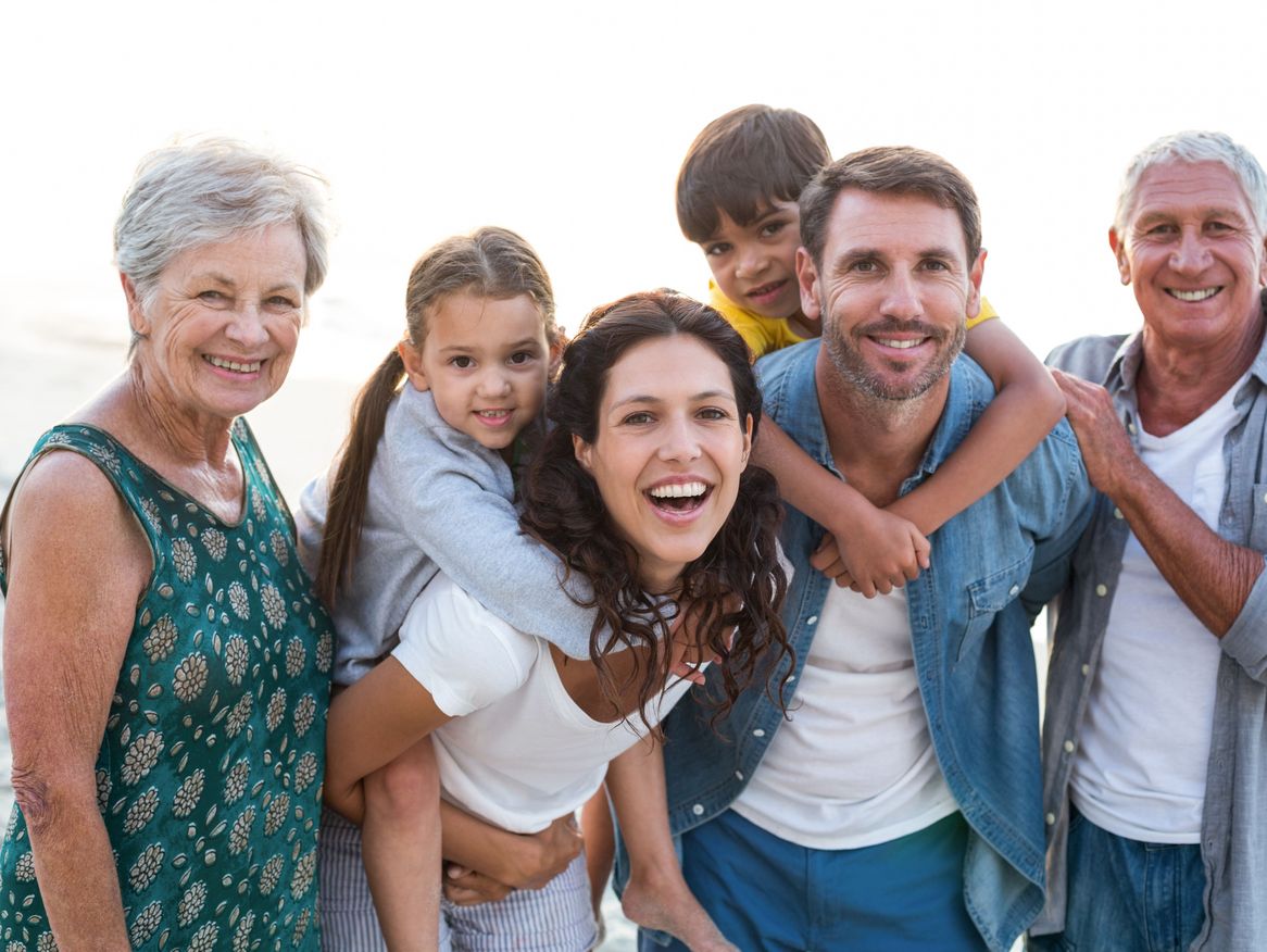 Eine fröhliche, generationsübergreifende Familie am Meer, mit Großeltern, Eltern und Kindern, die gemeinsam lachen und den Moment genießen. Die Nähe zum Wasser und die offenen Gesichter strahlen Freude und Familienzusammenhalt aus.