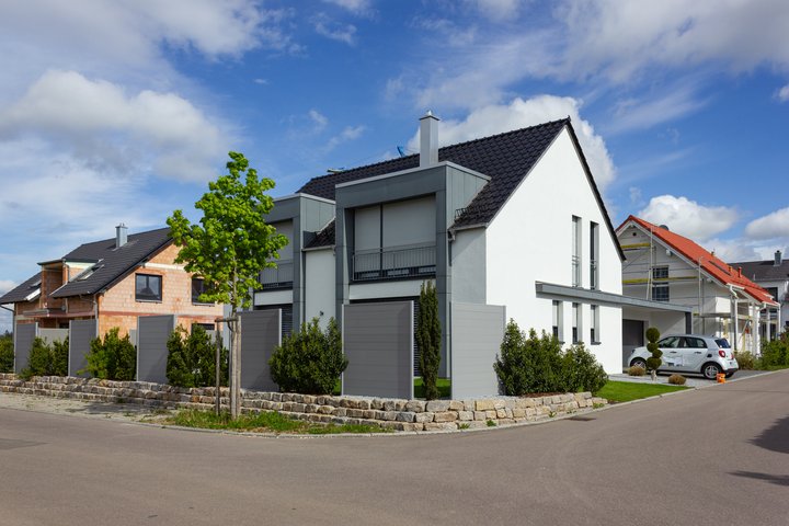 Moderne Wohnhäuser mit sauberen Linien, Giebeldächern und gepflegten Vorgärten in einer ruhigen Vorstadtsiedlung an einem sonnigen Tag mit einigen Wolken am blauen Himmel.