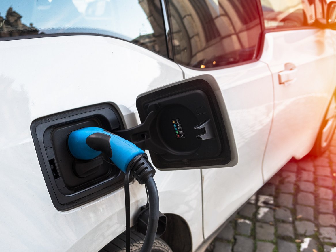 Ein weißes Elektroauto wird an einer öffentlichen Ladestation mit einem blauen Ladekabel aufgeladen, ein Szenario, das für die zunehmende Verbreitung von Elektromobilität steht.