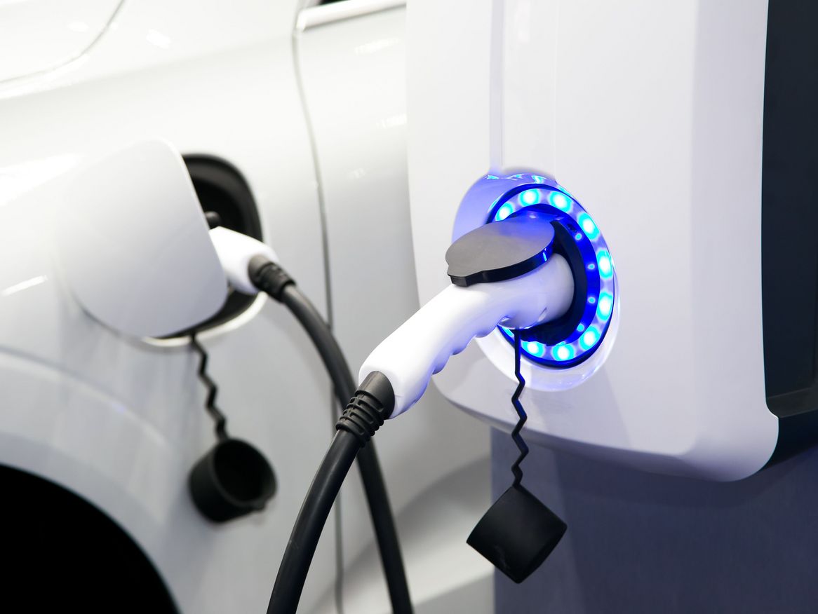 Ein Elektroauto wird an einer öffentlichen Ladestation geladen. Der Ladepunkt leuchtet blau, was den Ladevorgang anzeigt. Es ist ein Bild, das die steigende Nutzung von Elektromobilität und die zugängliche Ladeinfrastruktur darstellt.