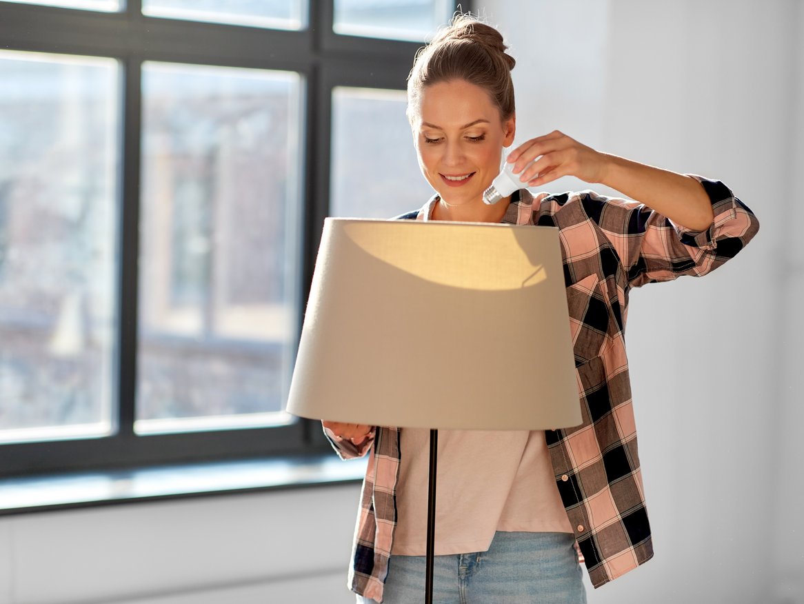 Eine junge Frau richtet eine moderne Stehleuchte ein und scheint das Design ihres Raumes zu überdenken oder zu verändern. Die Kombination aus ihrer lässigen Kleidung und dem stylischen Interieur deutet auf ein gemütliches, aber trendbewusstes Zuhause hin.