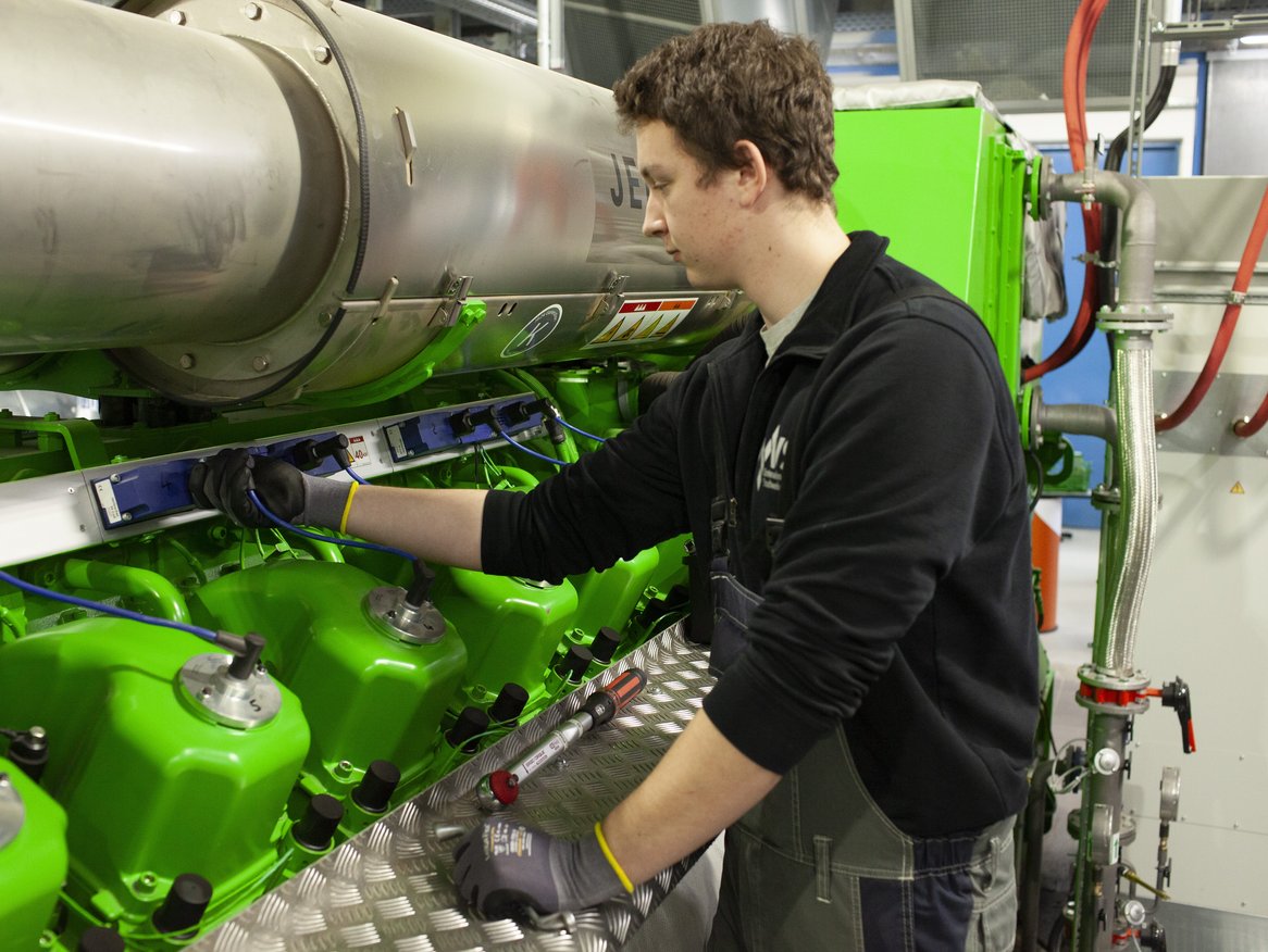 Industriearbeiter in Arbeitskleidung bedient Maschinen in einer Fabrikhalle, fokussiert auf die Einstellung eines großen grünen Maschinenteils