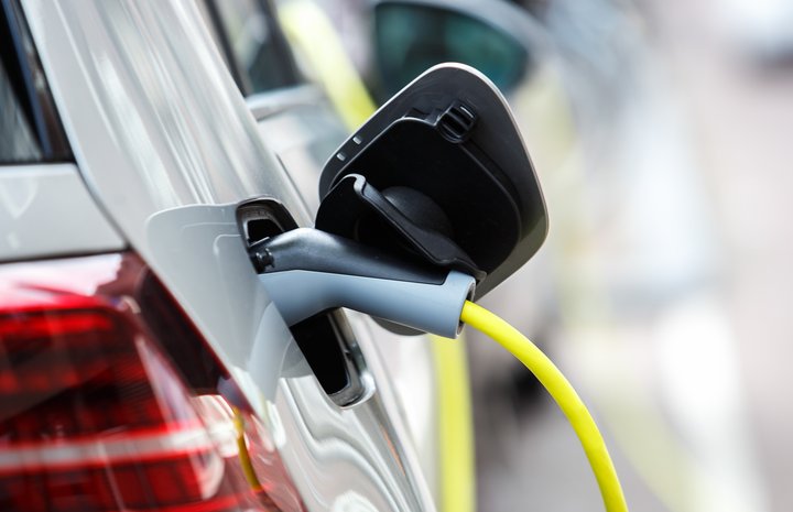 Ein Elektroauto wird aufgeladen, wobei das Ladekabel fest am Fahrzeug angeschlossen ist. Der Ladeanschluss leuchtet, was darauf hinweist, dass der Ladevorgang aktiv ist. Dieses Bild veranschaulicht den praktischen Aspekt der Elektromobilität im Alltag.