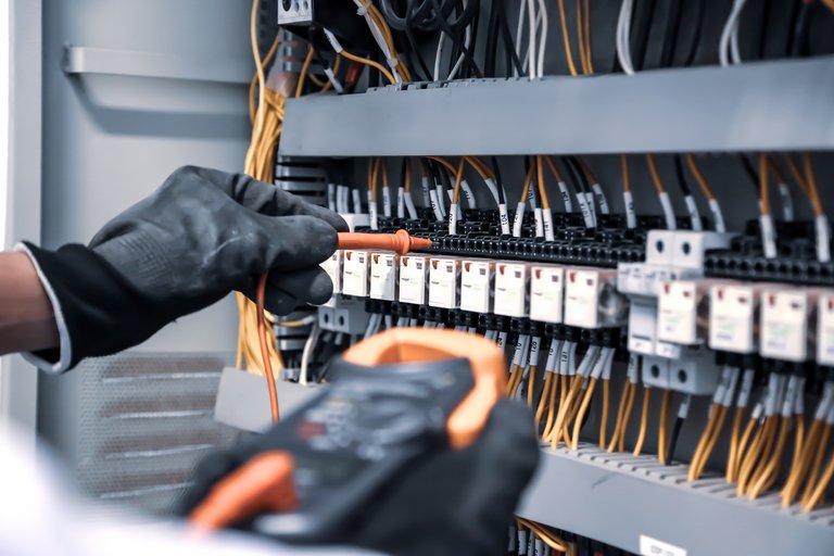 Detailaufnahme der Hände eines Elektrikers in Schutzhandschuhen, der an einer Schalttafel mit Kabeln und Sicherungselementen arbeitet.
