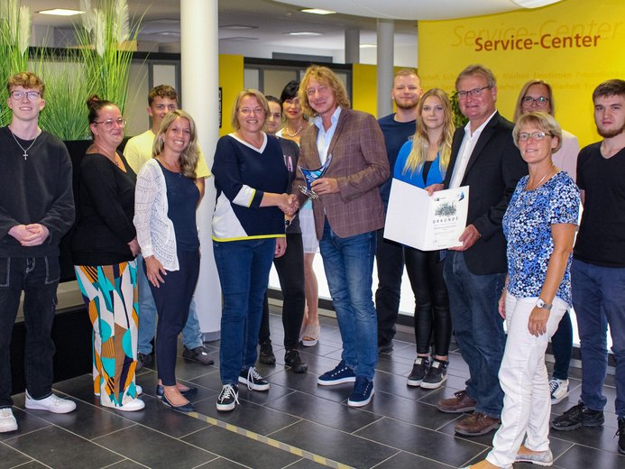 Eine Gruppe von Mitarbeitern der Stadtwerke Stralsund posiert stolz mit einer Auszeichnung für den '2023 Top Ausbildungsbetrieb', in einem Büro mit auffälligen gelben Wänden