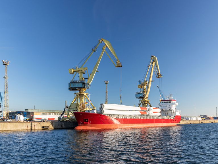 Ein rotes Schiff angedockt an einem Hafen mit zwei großen Hafenkränen im Hintergrund unter klarem blauen Himmel.