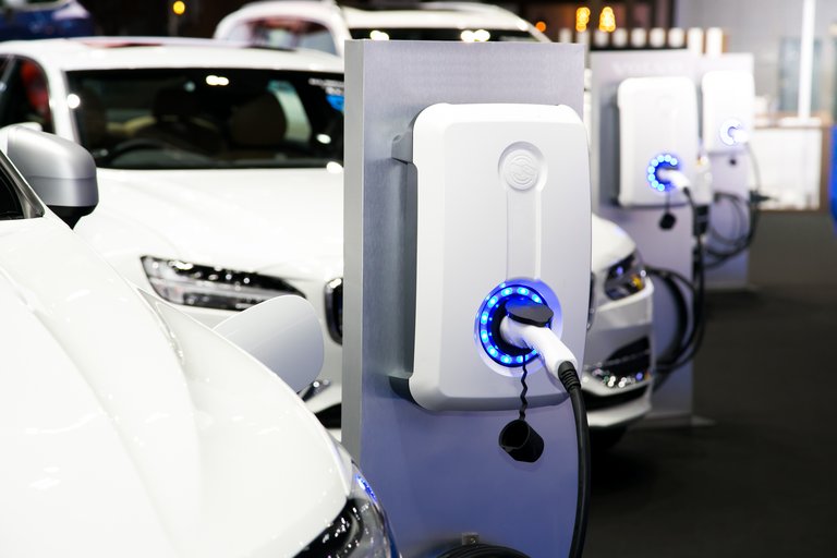 Eine Reihe von Elektroautos, die an Ladesäulen in einem Parkhaus aufgeladen werden, mit sichtbaren blauen Lichtern, die den Ladezustand anzeigen – ein fortschrittliches Bild urbaner Elektromobilität.
