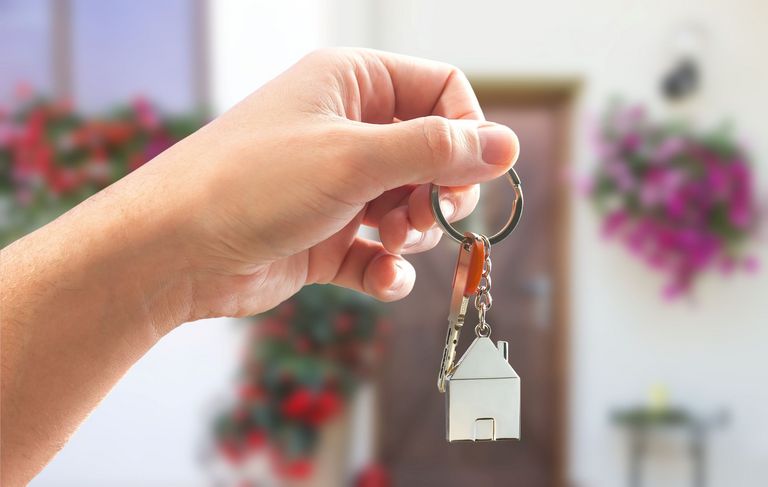 Eine Hand hält eine einen Schlüssel in der Hand, an dem ein kleines Haus zu sehen ist.