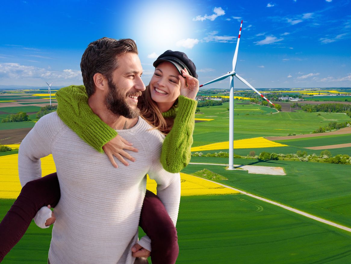 Ein Mann und eine Frau sind vor einem Panoramalandschaftsbild mit einer Windkraftanlage zu sehen.