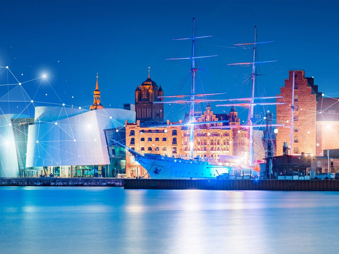 Eine Panoramaansicht einer beleuchteten Hafenstadt bei Nacht, mit einem Schiff im Vordergrund und einer Verbindung aus Lichtpunkten über dem Stadtbild, was auf Vernetzung und digitale Technologie hinweist.