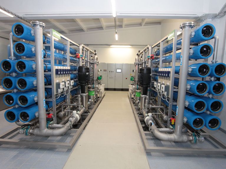 Innenansicht eines Wasseraufbereitungsraums mit mehreren Reihen von blauen Umkehrosmosefiltern und verbundenen Rohrleitungen.