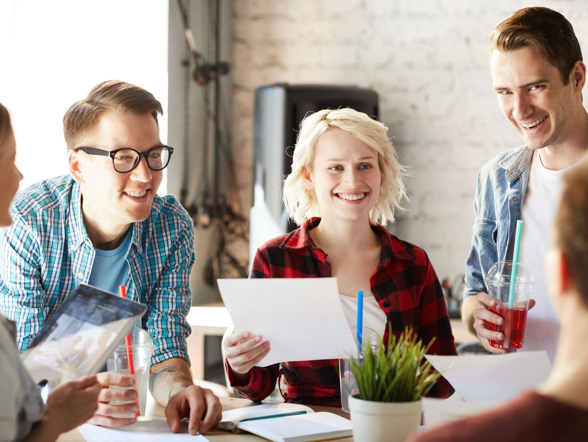 Eine Gruppe von lächelnden Kollegen in legerer Kleidung, die sich in einer hellen, informellen Büroumgebung versammelt haben, um einen Moment freudiger Teamarbeit oder eine angenehme Pause zu genießen.